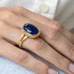 A gold ring featuring an oval blue sapphire, representing different neelam stone types